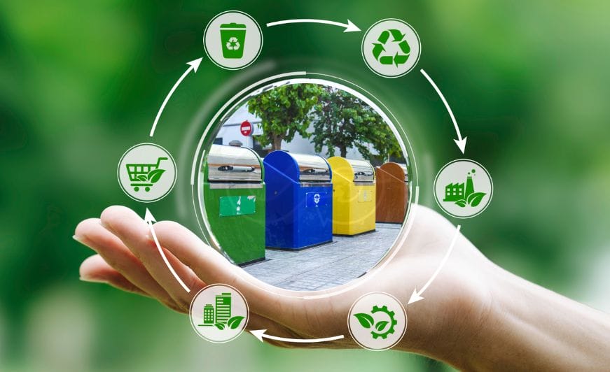 Eine Hand hält Symbole der Kreislaufwirtschaft um farbenfrohe Recyclingbehälter in Barcelona herum.