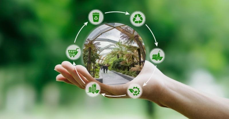 Economía circular en Londres: Una mano sosteniendo un símbolo de la economía circular de Londres, rodeada de iconos para el reciclaje, los edificios ecológicos, la reducción de residuos y las compras sostenibles, ilustrando el compromiso de Londres con las prácticas urbanas sostenibles.